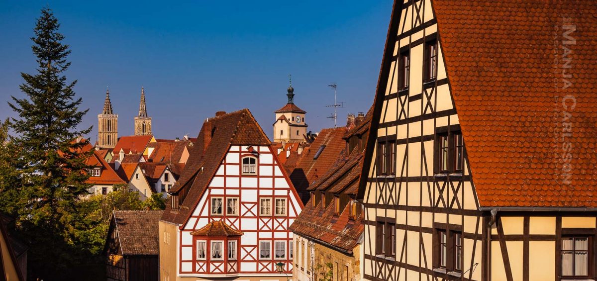 Rothenburg ob der Tauber - Auf der alten restaurierten Stadtmauer entlang laufend die Dächer und die hübschen Fachwerkhäuser anschauend bei morgendlichen schönen Sonnenlicht mit blauem Himmel