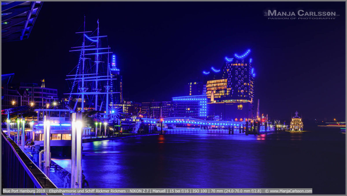 Blue Port Hamburg 2019 - Ausblick von den Landungsbrücken auf die blau erleuchtete Hamburger Flaniermeile entlang der Elbe. Zusehen sind das Museumsschiff Rickmer Rickmers und die Elbphilharmonie. Die Fenster der Elbphilharmonie erleuchten im orange. Die blauen Blue Port-Lichterstreifen verzieren die Gebäude und die Überseebrücke.